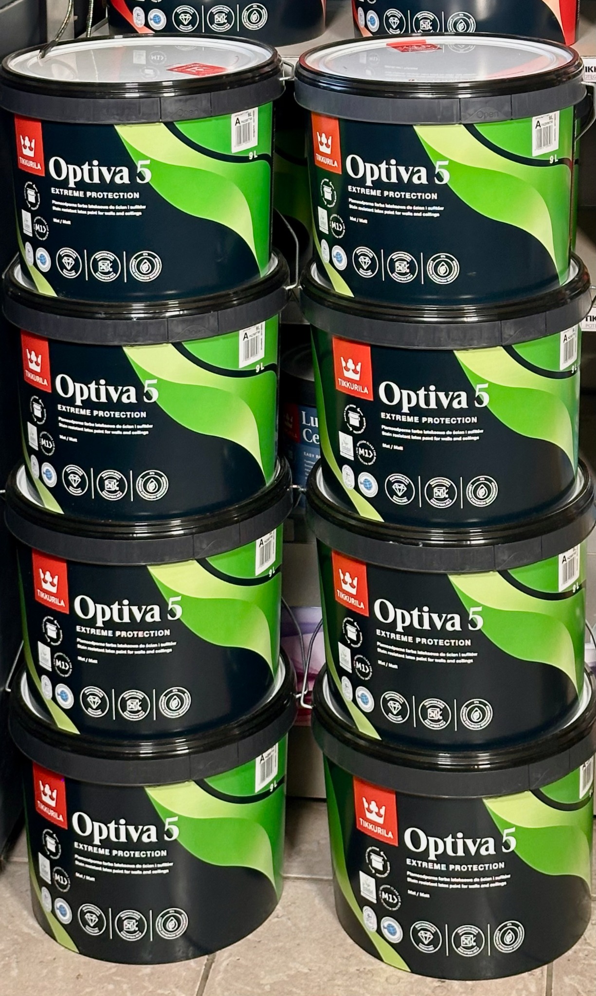 Stos czarnych wiader z zieloną farbą Tikkurila Optiva 5 Extreme Protection, widoczne etykiety z logo i informacjami o produkcie, ułożone w rzędach.