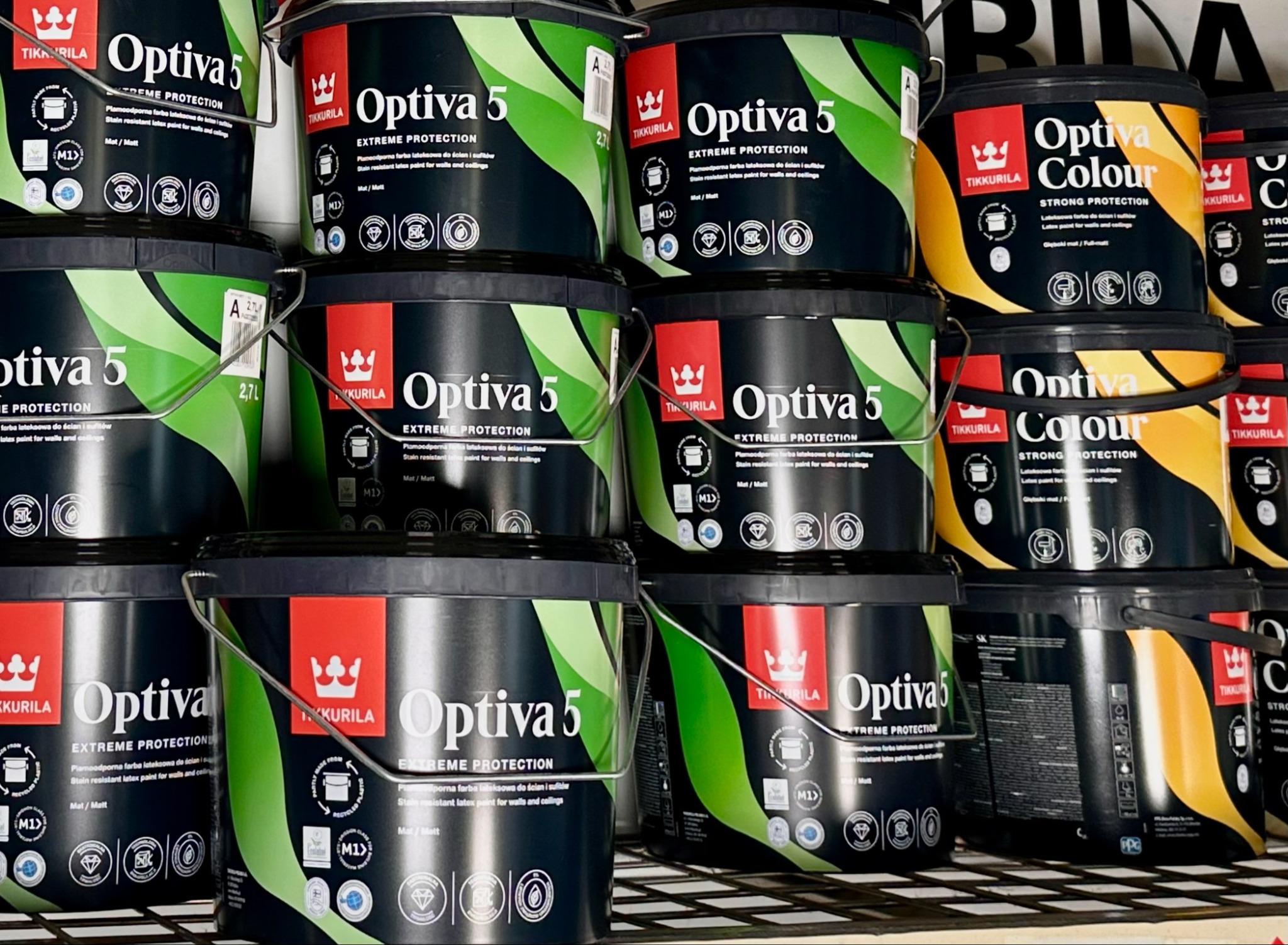 Stos czarnych puszek farby Tikkurila Optiva 5 i Optiva Colour na półce, widoczne etykiety z informacjami o produkcie i logo firmy.