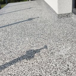 Elpox - Szara posadzka z czarno-białych kamyczków na balkonie, cień osoby fotografującej.