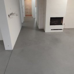 Elpox - Szara, gładka posadzka w nowym wnętrzu z kominkiem; widoczne niedokończone ściany i wystające przewody elektryczne.