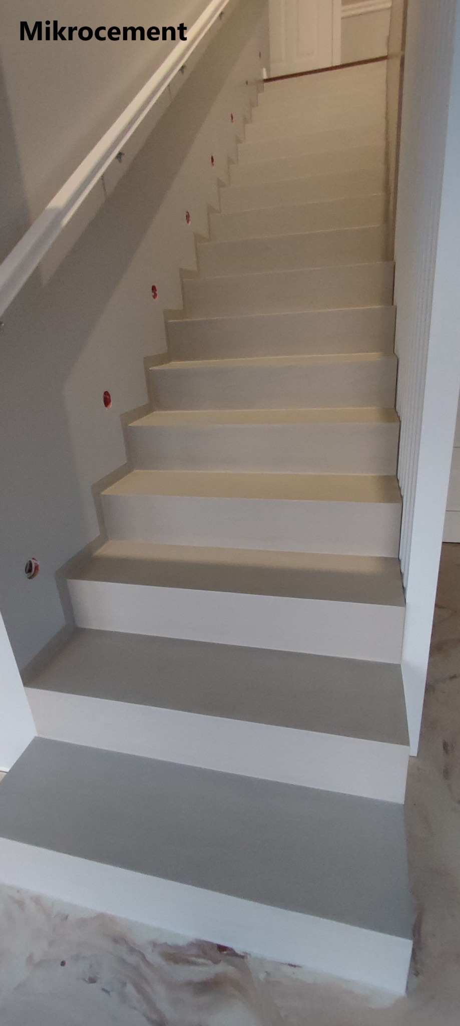 Schody wewnętrzne w Ełku wykończone jasnoszarym materiałem, prawdopodobnie na bazie cementu, z widocznymi punktami montażowymi oświetlenia na ścianie.