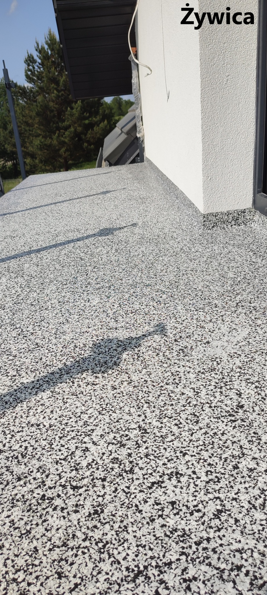 Szara posadzka z czarno-białych kamyczków na balkonie, cień osoby fotografującej.