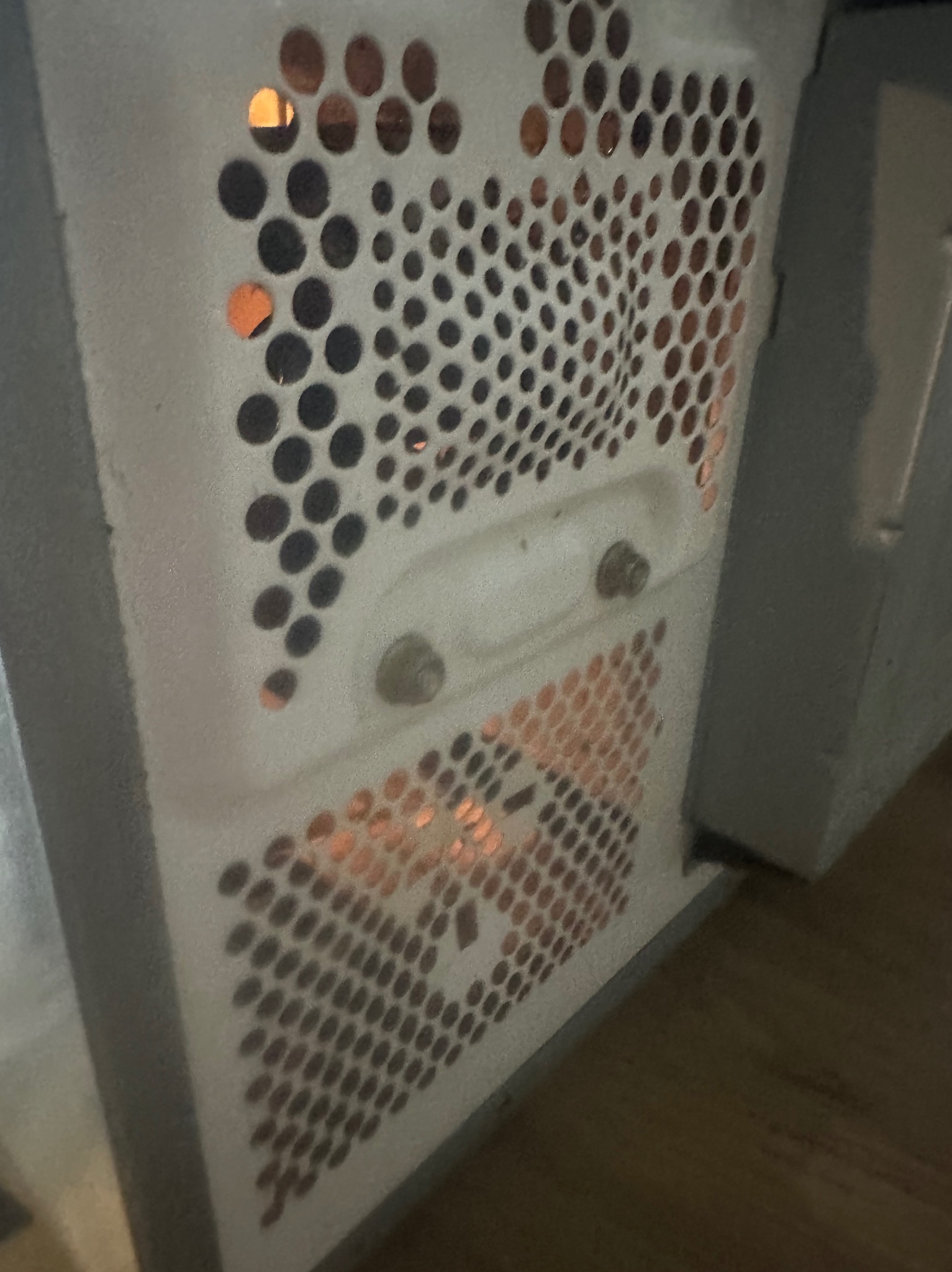 Boczny widok zakurzonej, białej obudowy komputera stacjonarnego z perforowaną powierzchnią i widocznymi śrubami montażowymi.