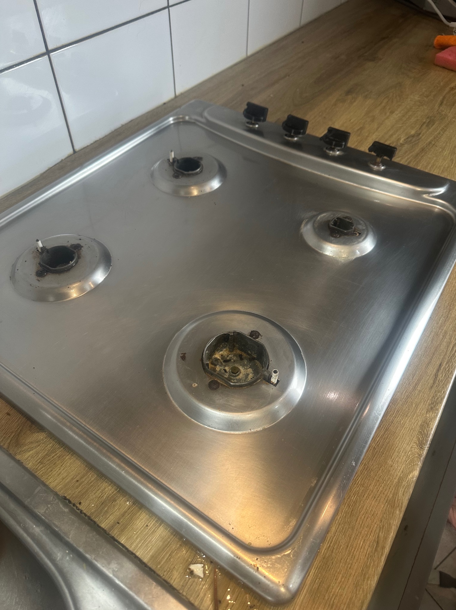 Brudna, metalowa płyta gazowa z czterema palnikami, wymagająca czyszczenia. Widoczne resztki jedzenia i zabrudzenia na palnikach i powierzchni płyty.