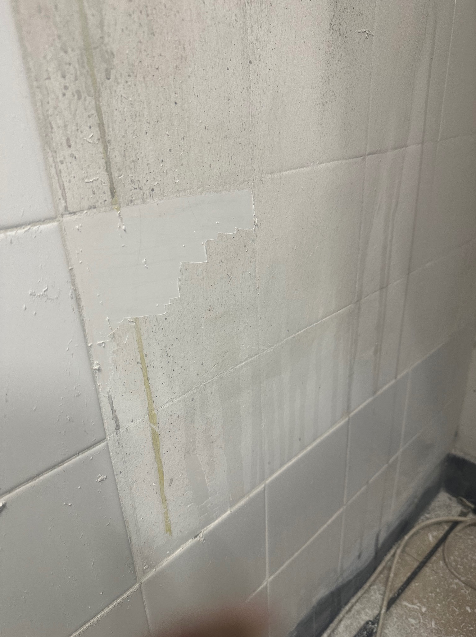 Fragment ściany z białych płytek po usunięciu zabrudzeń, z widocznymi smugami i resztkami po czyszczeniu, oraz fragmentem ściany z pozostałościami po remoncie.