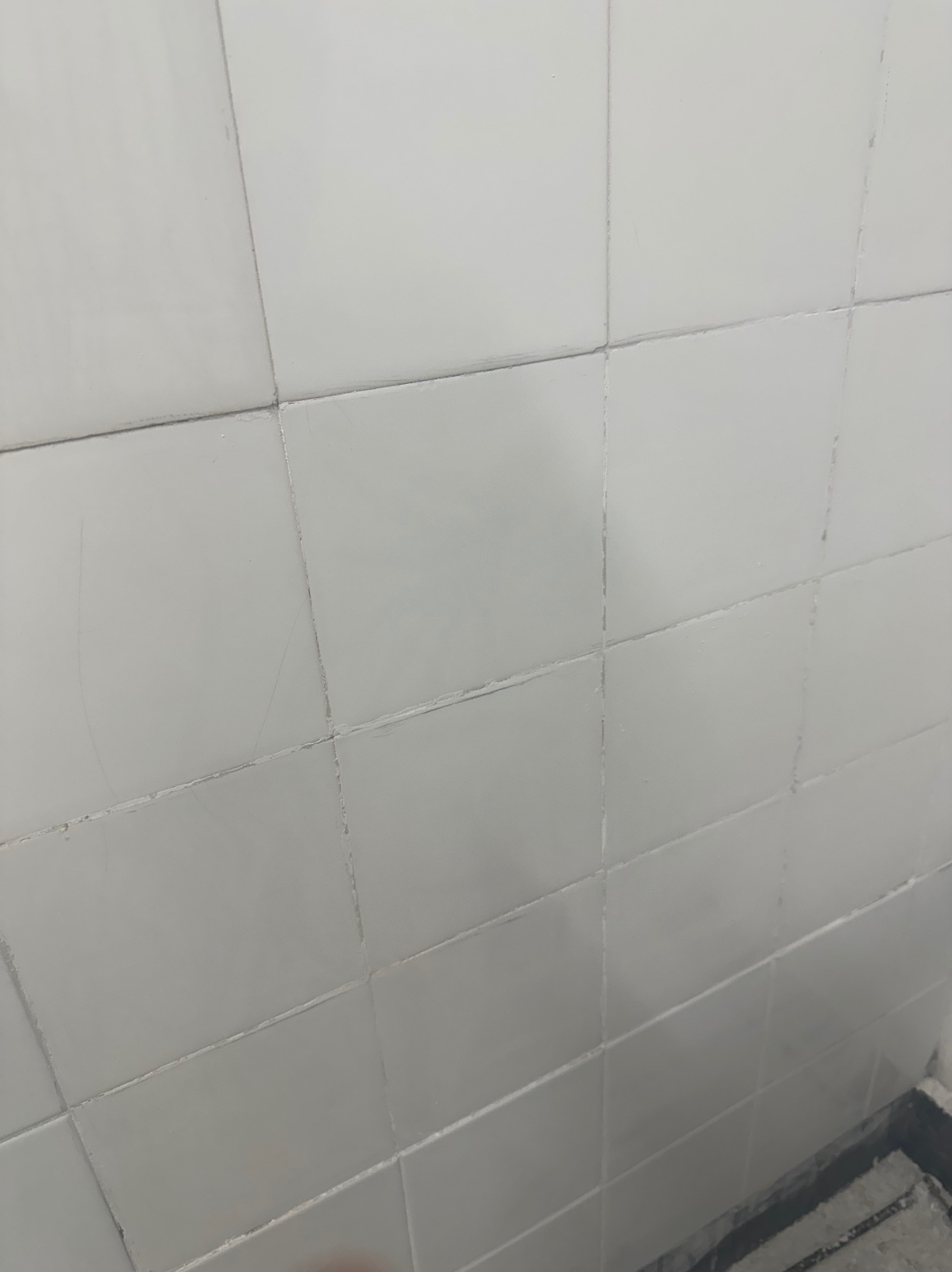 Brudne, białe płytki ścienne z widocznymi zabrudzeniami w fugach i zarysowaniami na powierzchni.