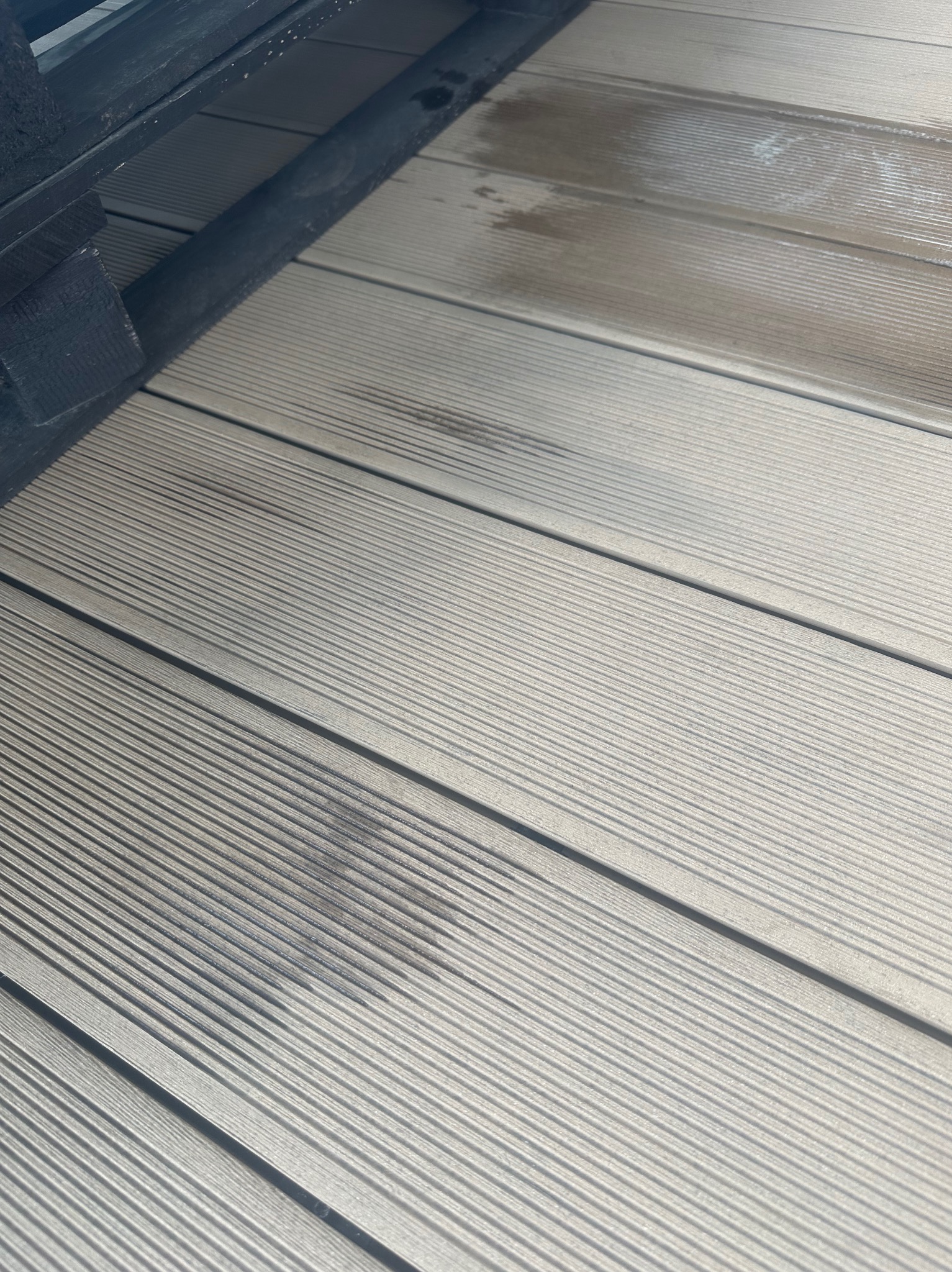 Szczegółowe zbliżenie na zabrudzoną, ryflowaną deskę tarasową z widocznymi plamami i zaciekami, sugerujące potrzebę czyszczenia powierzchni.