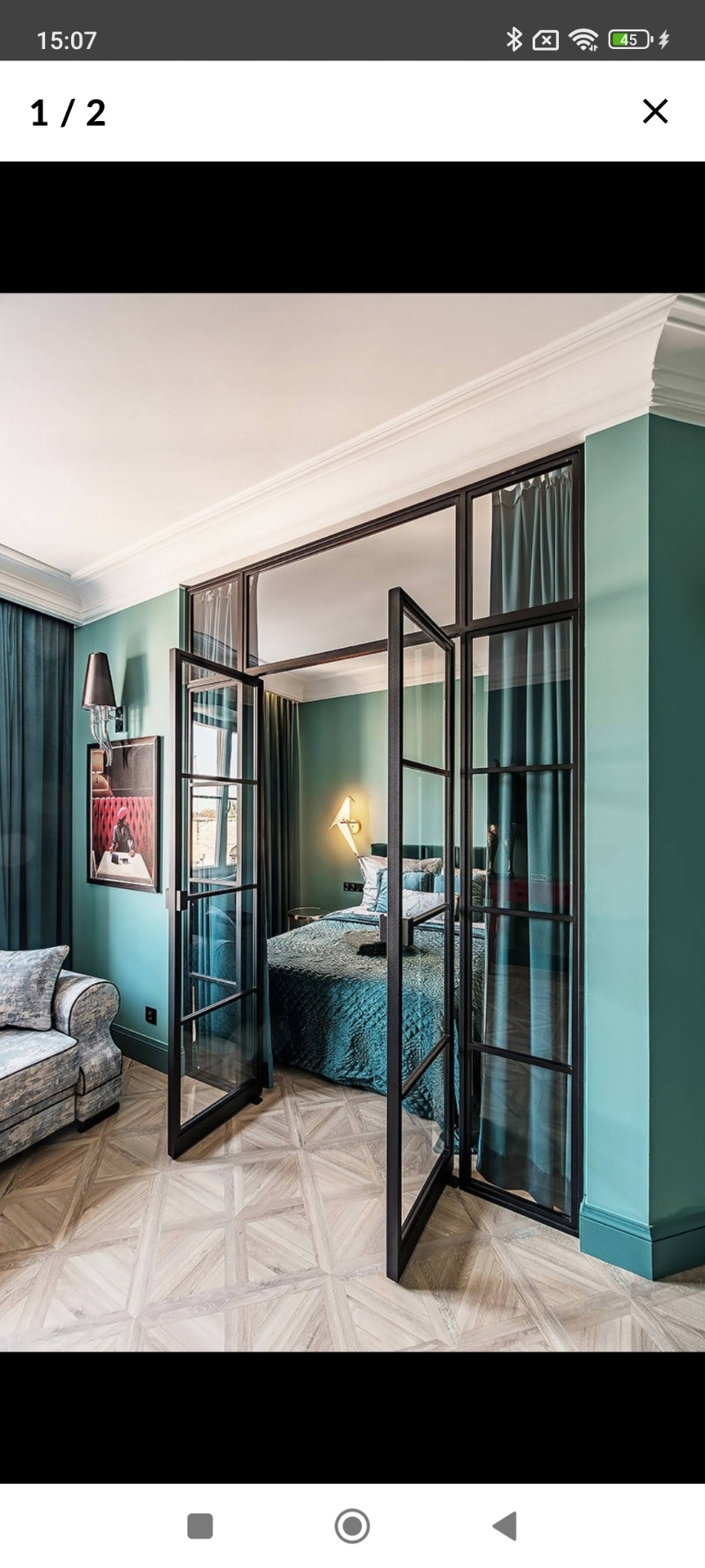 Eleganckie, szklane drzwi dwuskrzydłowe z czarną ramą oddzielają pokój. W tle widoczne łóżko i zasłony w odcieniach zieleni i błękitu. Parkiet w geometryczny wzór.