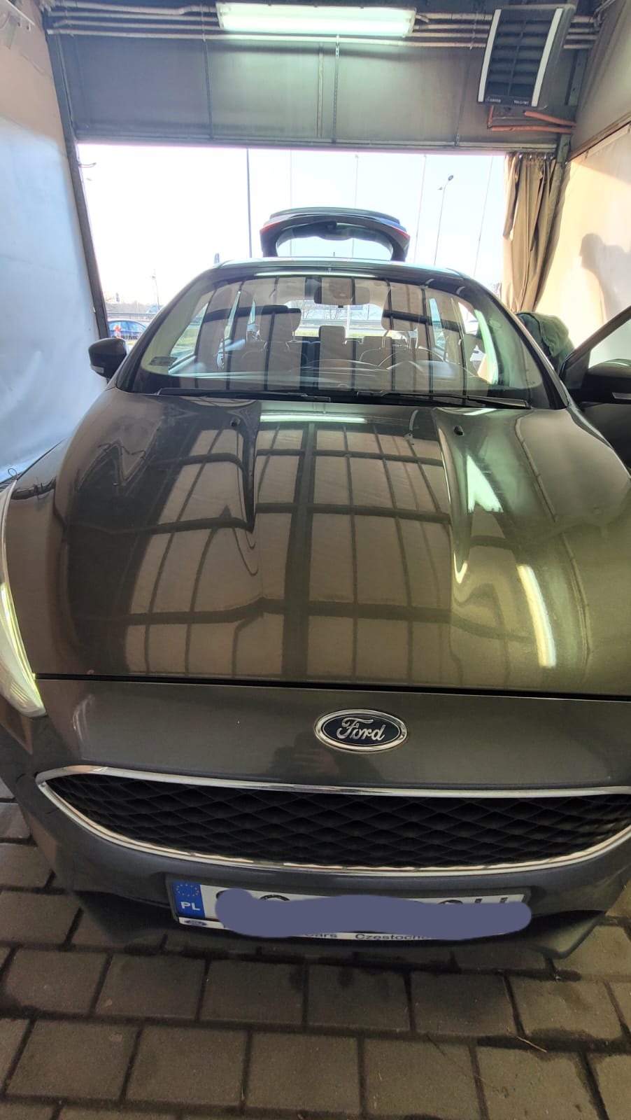 Szary Ford po umyciu w myjni automatycznej, widoczne refleksy świetlne na karoserii, otwarty bagażnik.