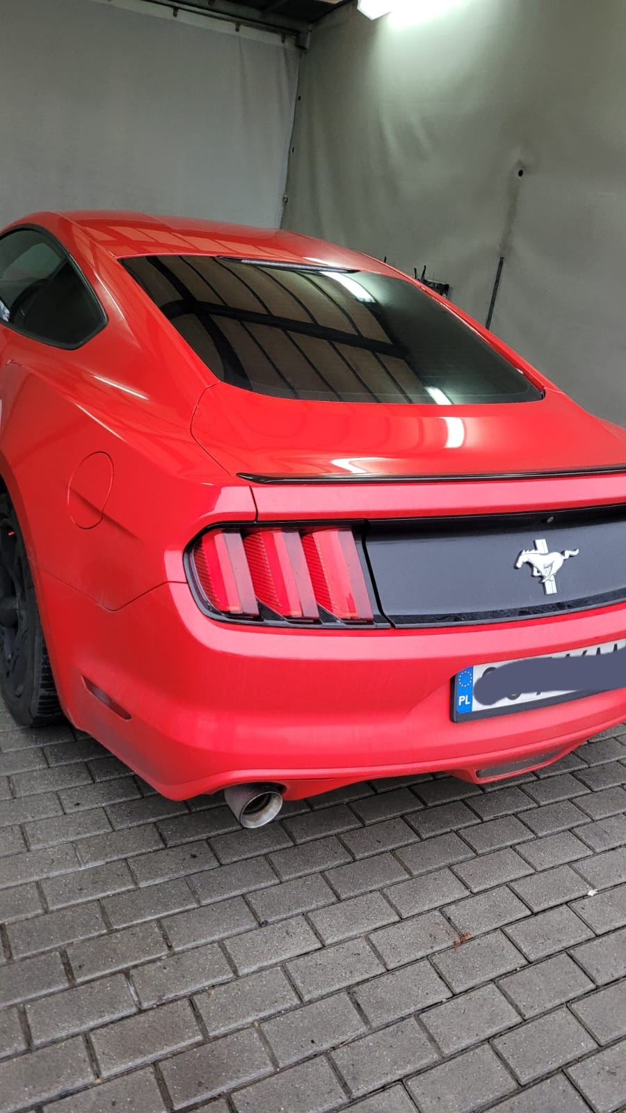 Czerwony samochód Ford Mustang po umyciu, widok z tyłu, na kostce brukowej, z widocznym wydechem i lampami