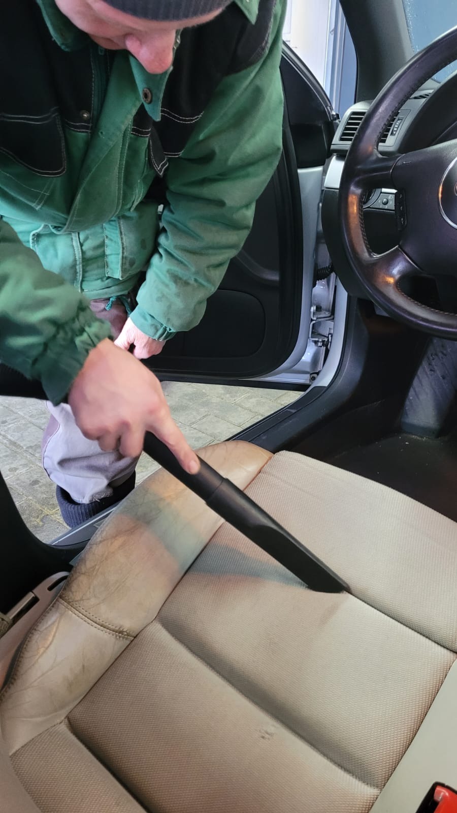 Czyszczenie jasnej, skórzanej tapicerki samochodowej odkurzaczem z wąską ssawką. Widoczne zabrudzenia na siedzeniu przed czyszczeniem.