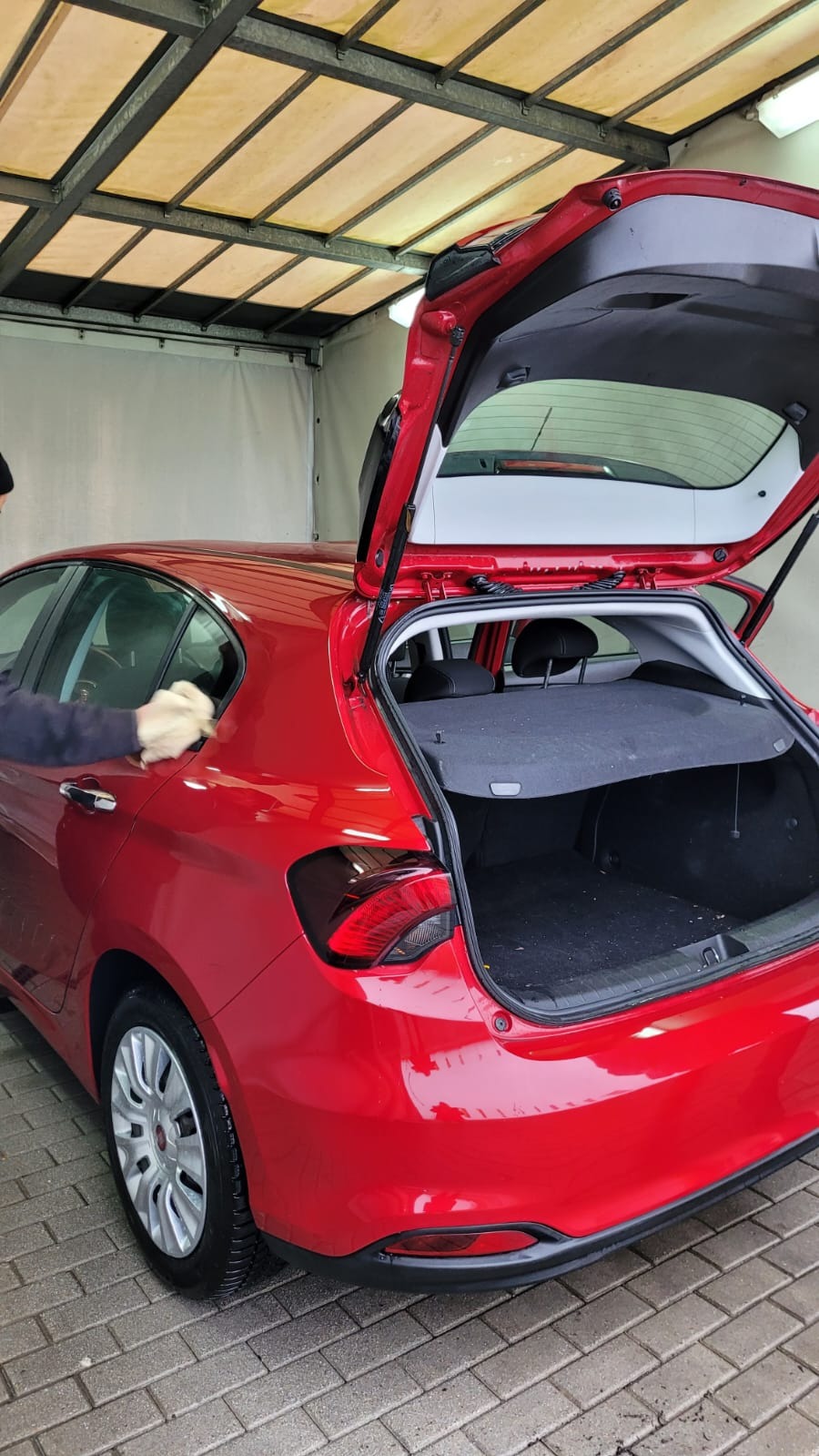 Czerwony samochód typu hatchback z otwartą klapą bagażnika, czyszczony z zewnątrz pod zadaszeniem myjni.