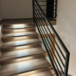 Nowoczesne schody drewniane z podświetleniem LED i czarną, minimalistyczną poręczą z płaskich profili stalowych.