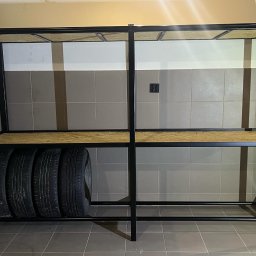 Stal fox - Metalowy regał z drewnianymi półkami, na których leżą opony samochodowe, ustawiony w pomieszczeniu wyłożonym szarymi płytkami.