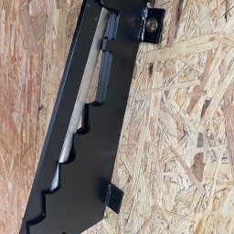 Stal fox - Czarny, metalowy element konstrukcyjny z wycięciami, przymocowany do płyty OSB za pomocą śrub i zawleczki, widoczne detale mocowania.