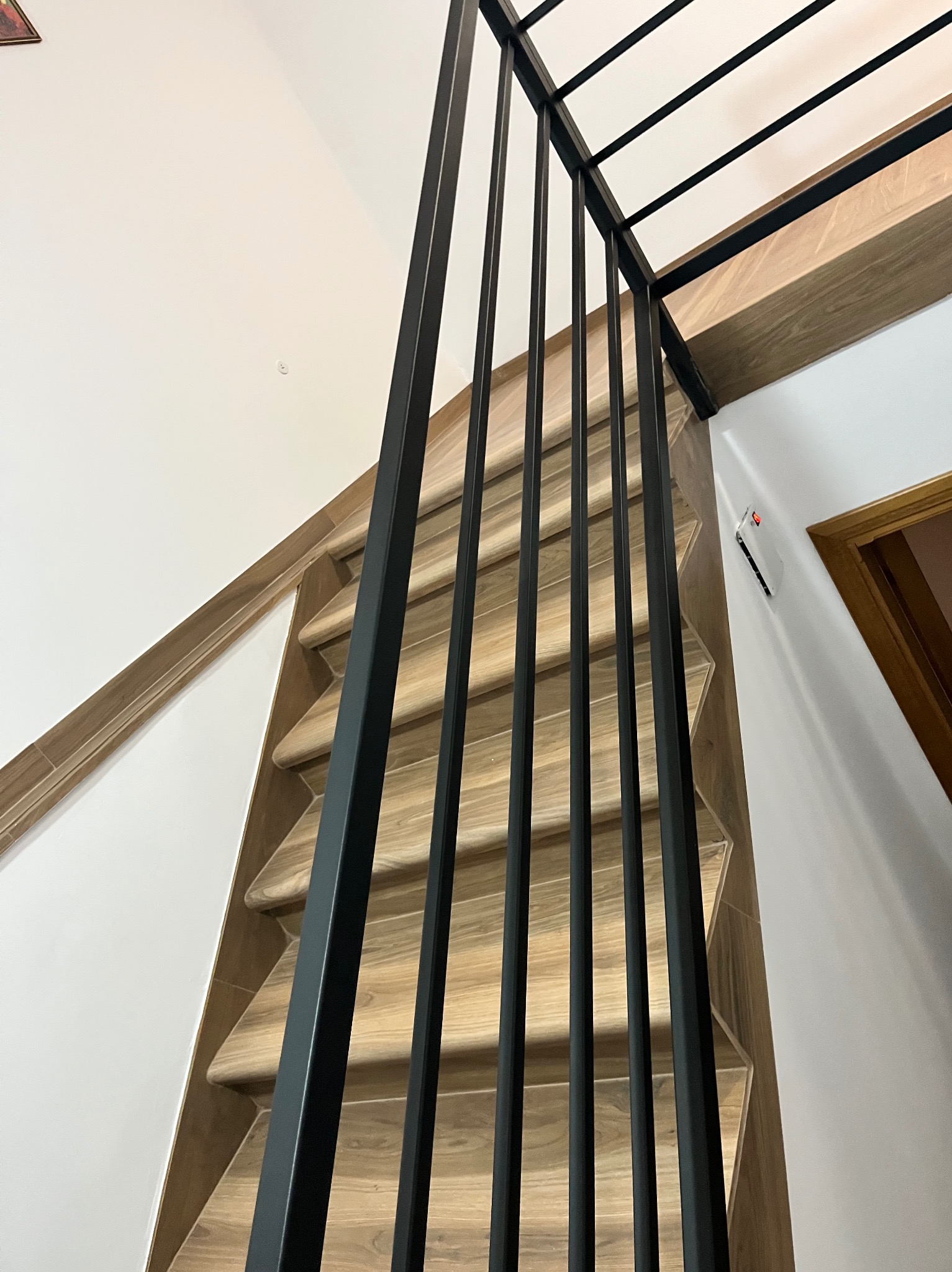 Nowoczesne, czarne, metalowe słupki balustrady schodowej z drewnopodobnymi stopniami, widok z dołu, minimalistyczny design.