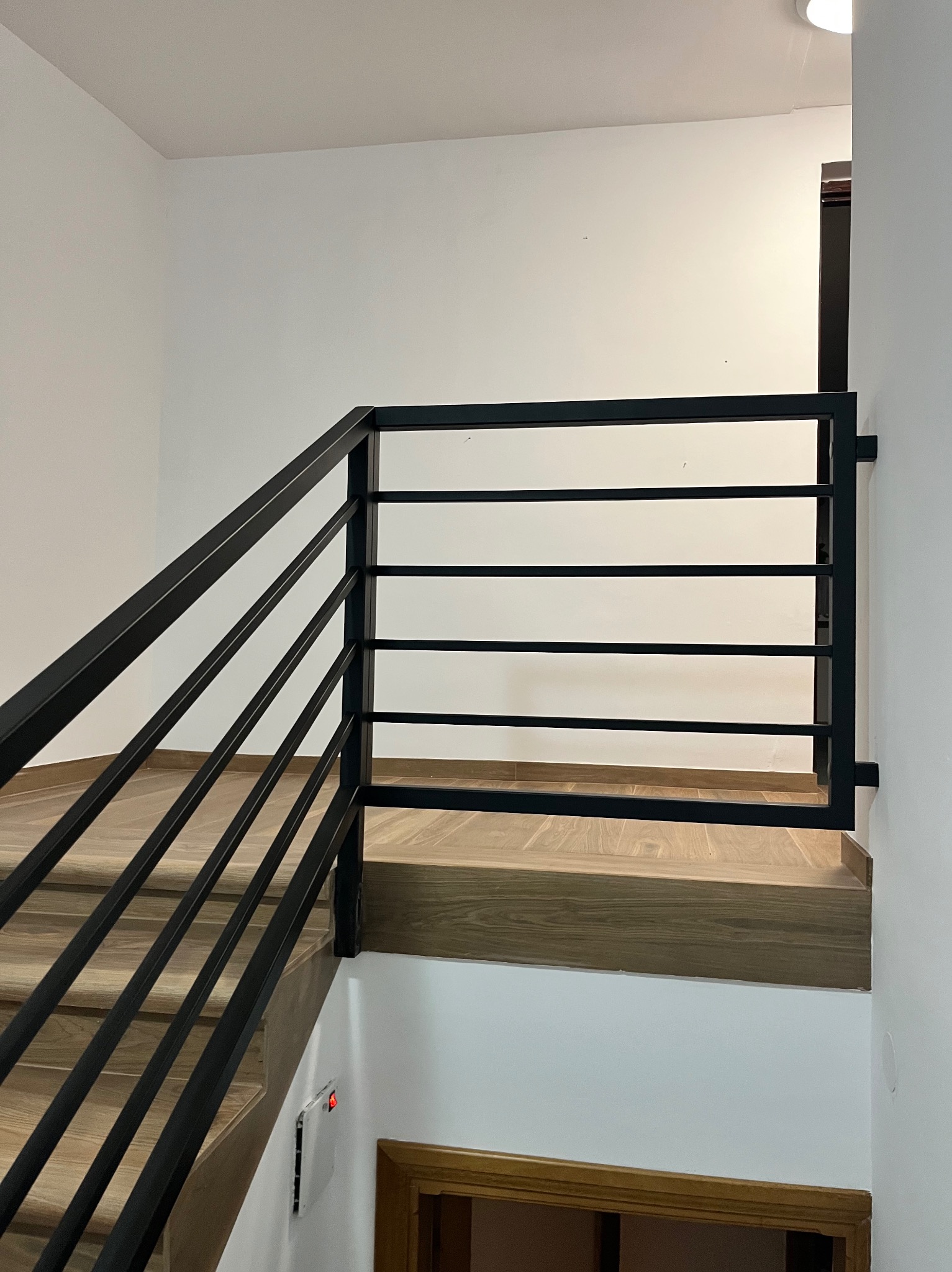 Nowoczesne czarne poręcze schodowe z poziomymi szczeblami, zamontowane na drewnianych schodach w jasnym wnętrzu.