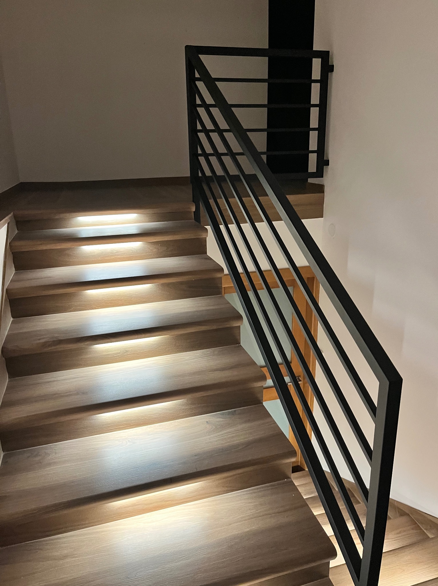 Nowoczesne schody drewniane z podświetleniem LED i czarną, minimalistyczną poręczą z płaskich profili stalowych.