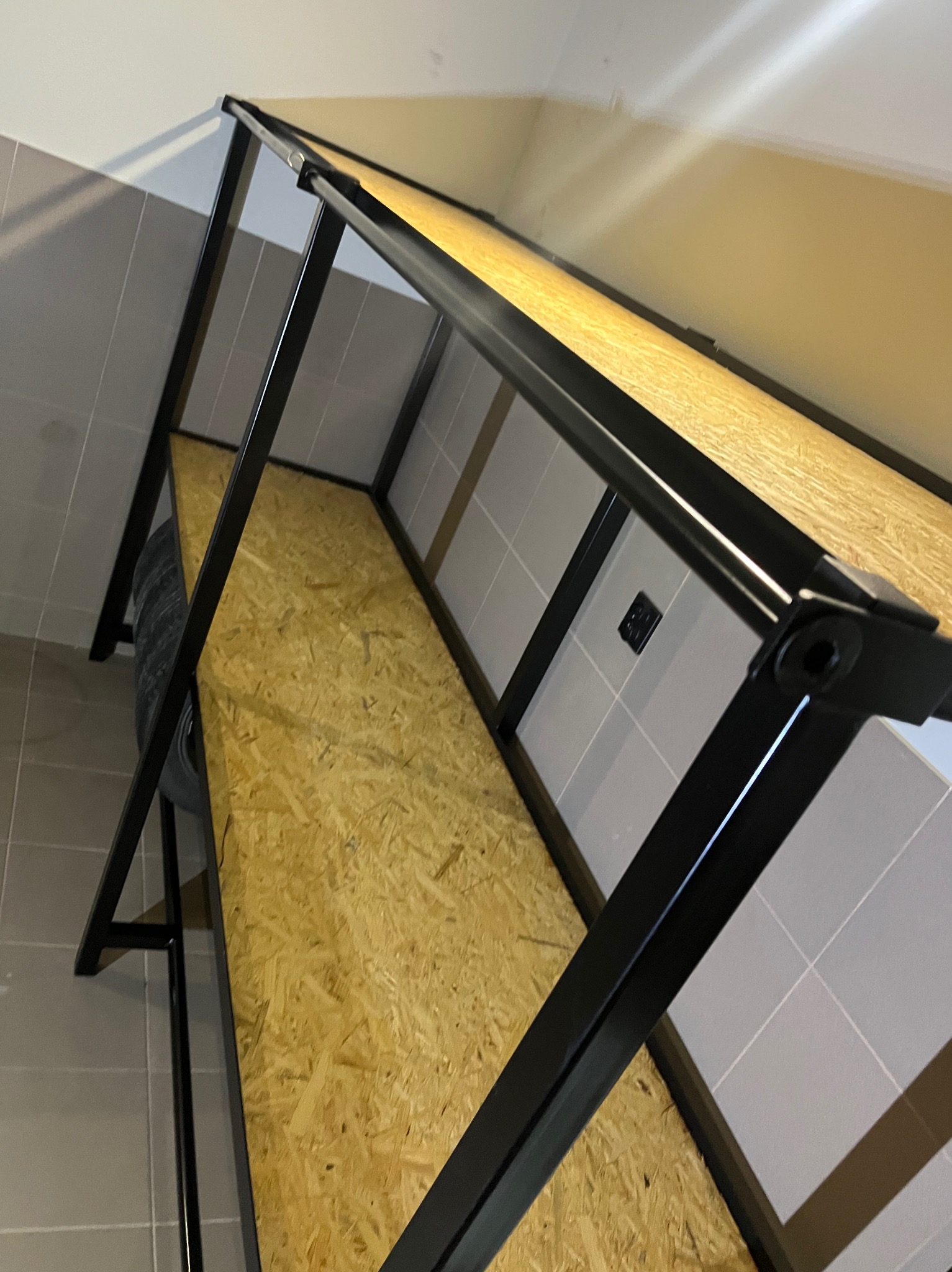 Metalowa konstrukcja z wypełnieniem z płyty OSB, prawdopodobnie w trakcie montażu, widoczne elementy spawane i mocowania śrubowe, tło stanowi ściana z płytek.