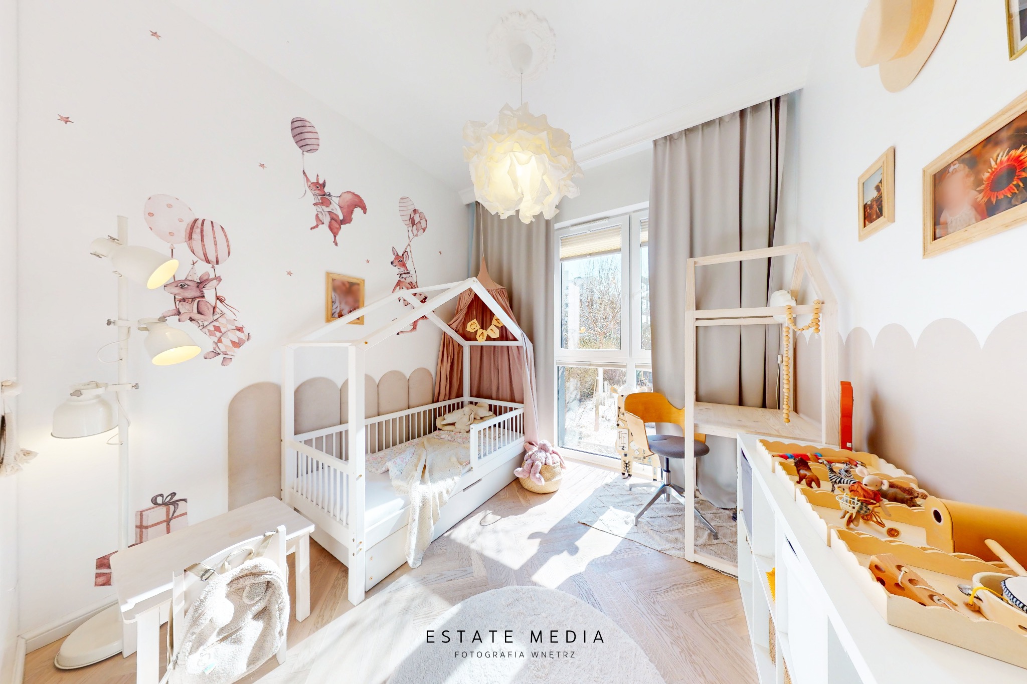 Jasny pokój dziecięcy z łóżkiem w kształcie domku, biurkiem, zabawkami i dekoracjami ściennymi z motywem zwierząt i balonów.