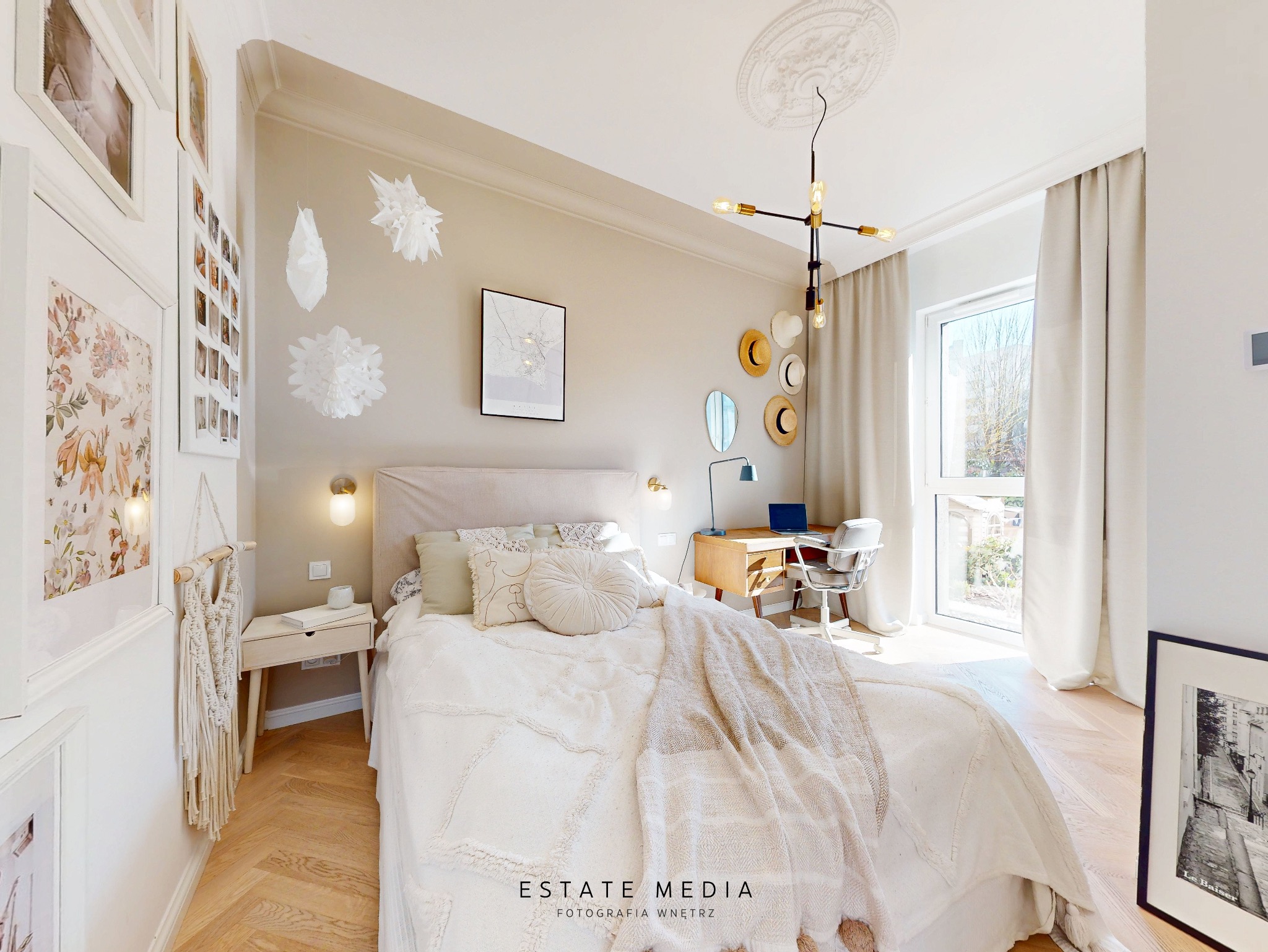 Jasna sypialnia z łóżkiem, biurkiem przy oknie i dekoracjami na ścianach, w stylu boho.