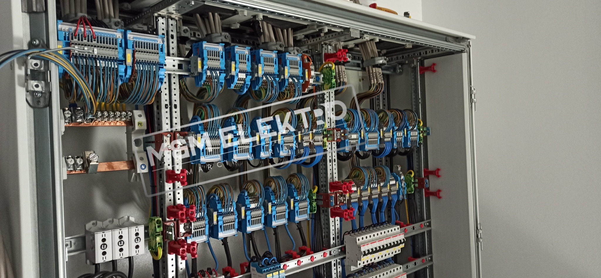 Otwarta szafa elektryczna z licznymi przewodami, bezpiecznikami i złączkami, uporządkowana instalacja w szynach montażowych.