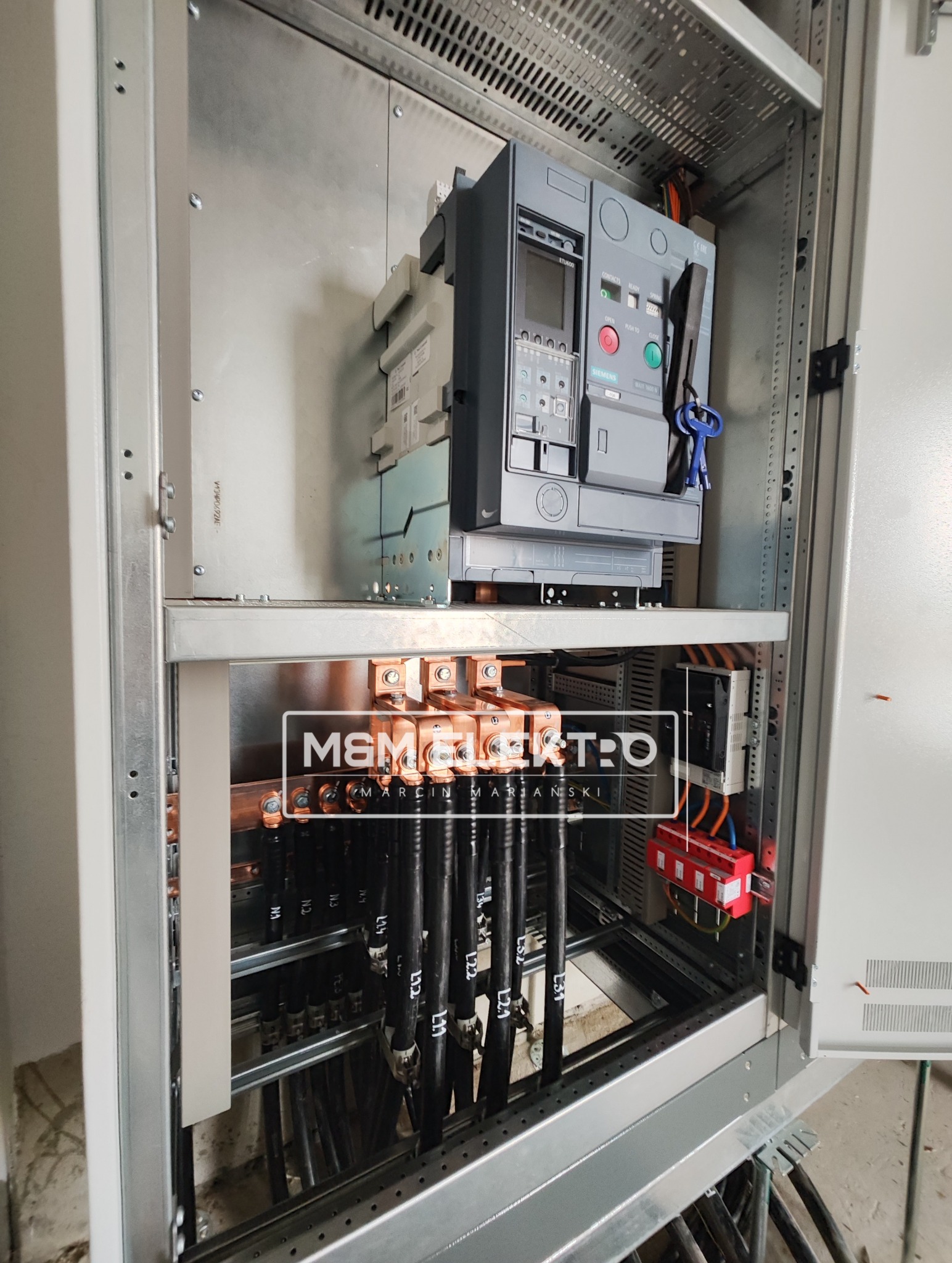 Otwarta szafa elektryczna z zainstalowanym wyłącznikiem mocy Siemens ETU600, miedzianymi szynami zbiorczymi i czarnymi kablami oznaczonymi L1, L2, L3; widoczne logo firmy M&M Elektro.