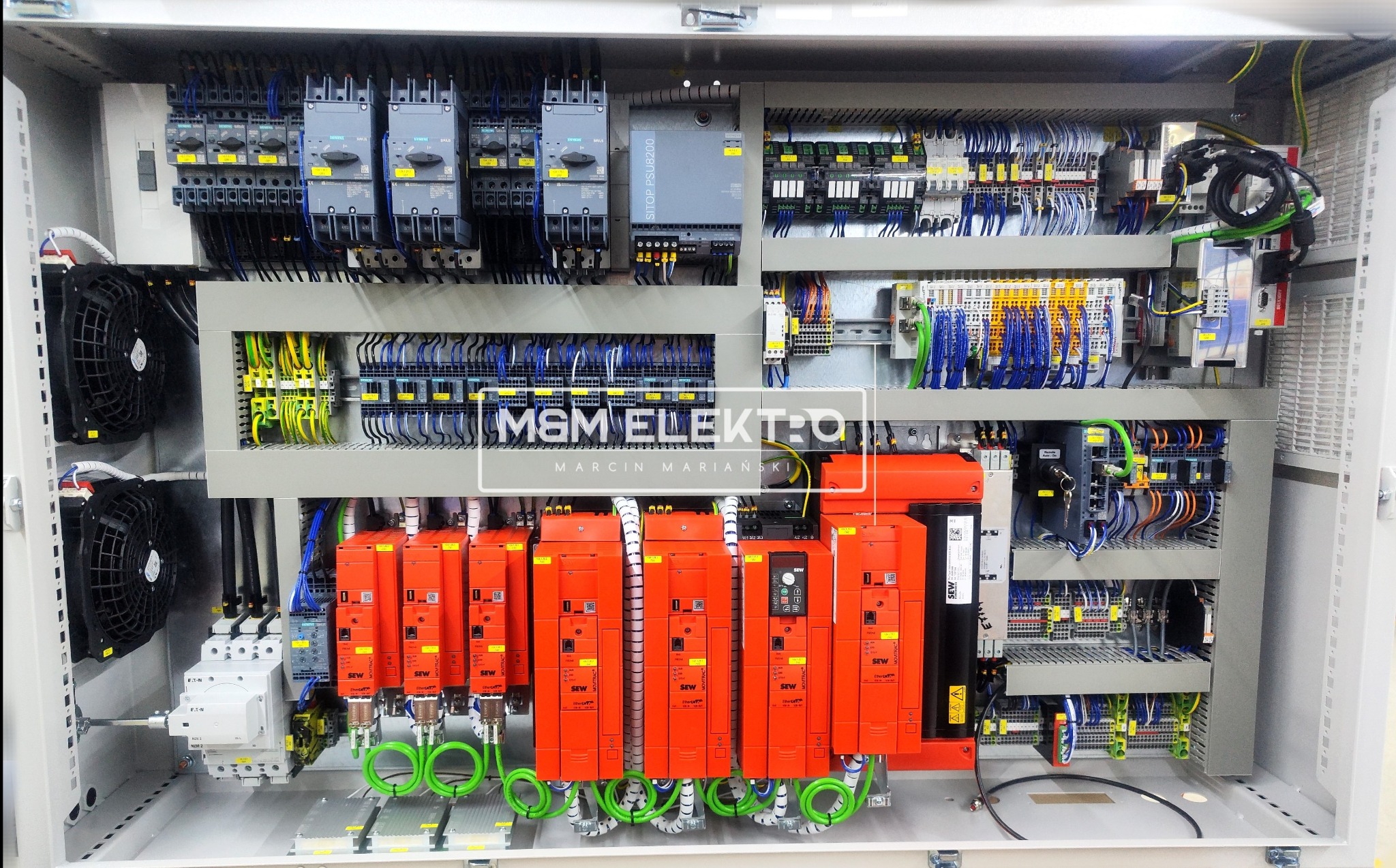 Otwarta szafa sterownicza z licznymi elementami elektrycznymi, w tym sterownikami SEW w pomarańczowych obudowach, zabezpieczeniami Siemens, wentylatorami chłodzącymi i bogatym okablowaniem...
