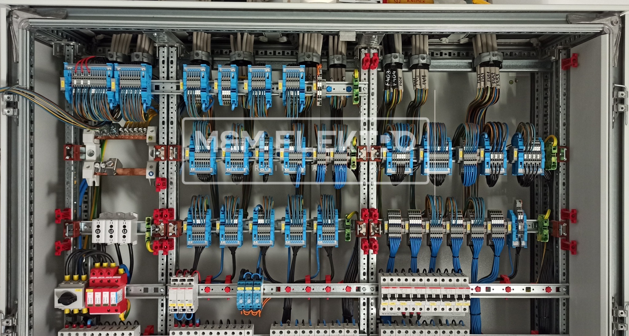 Rozdzielnica elektryczna z licznymi niebieskimi modułami, starannie ułożonymi kablami i zabezpieczeniami, zamontowana w metalowej obudowie z szynami DIN.