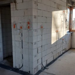 J&L - Surowy stan budynku z widocznymi przewodami elektrycznymi w peszlach przy podłodze i puszkami instalacyjnymi w ścianach z betonu komórkowego.