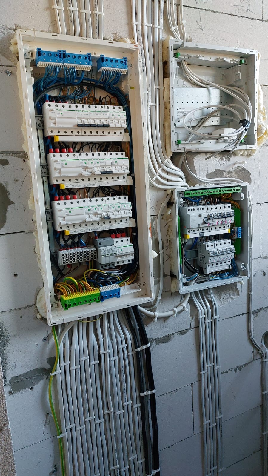 Rozdzielnice elektryczne w trakcie montażu na ścianie z betonu komórkowego, widoczne liczne przewody i zabezpieczenia, piana montażowa uszczelniająca obudowy.