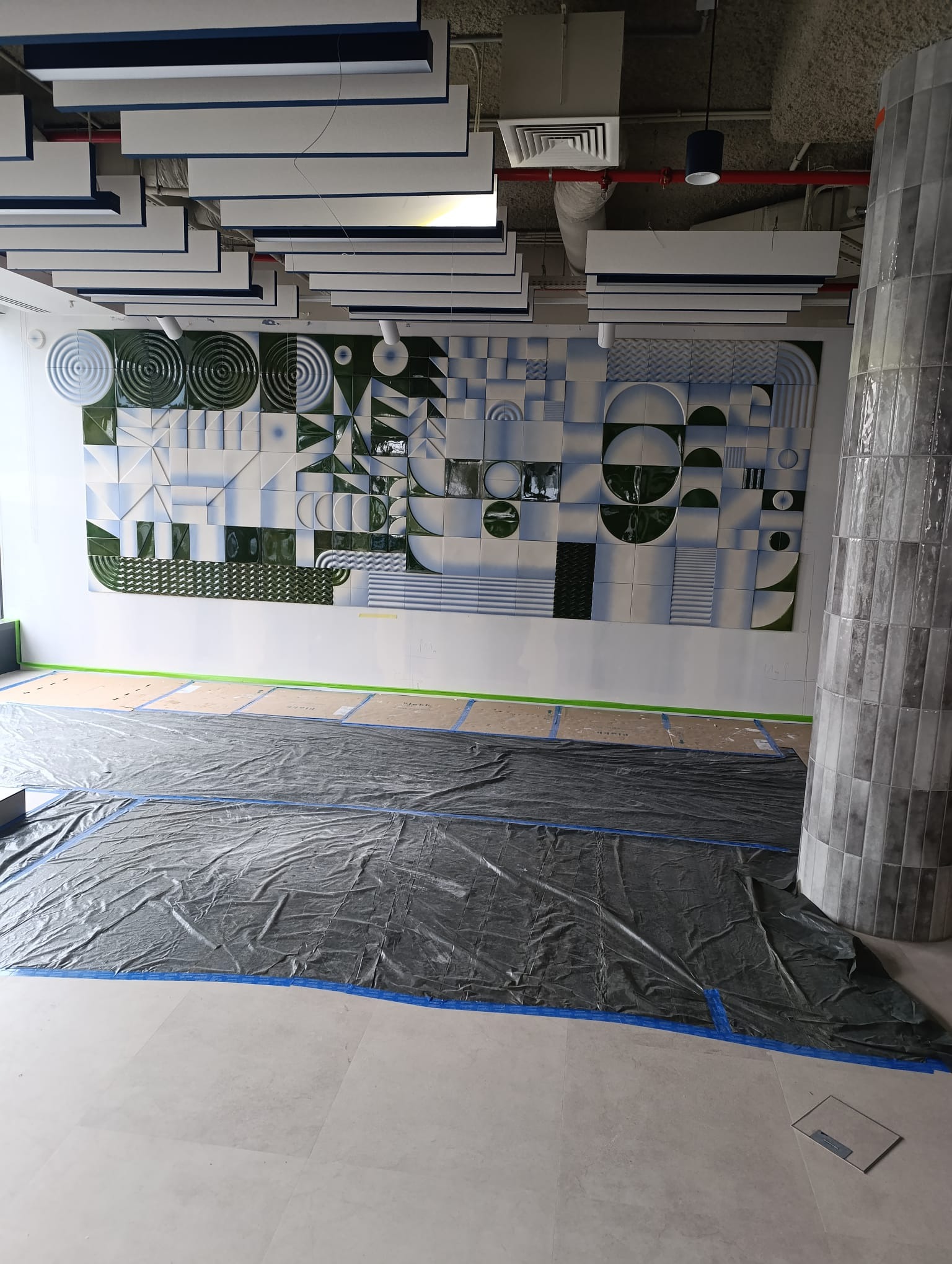 Ściana z unikalną mozaiką ceramiczną w odcieniach bieli, błękitu i zieleni. Podłoga zabezpieczona folią malarską. Kolumna wykończona szarą glazurą.