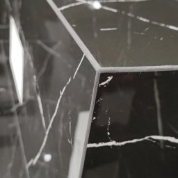 OK-BUD - Fragment umywalki z czarnego marmuru z białymi żyłami, widoczny ostry kant i odbicie światła.