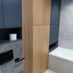 OK-BUD - Nowoczesna łazienka z zabudową meblową w odcieniach szarości, granatu i drewna, widoczna toaleta, wanna i grzejnik drabinkowy, z rolką papieru toaletowego na półce.