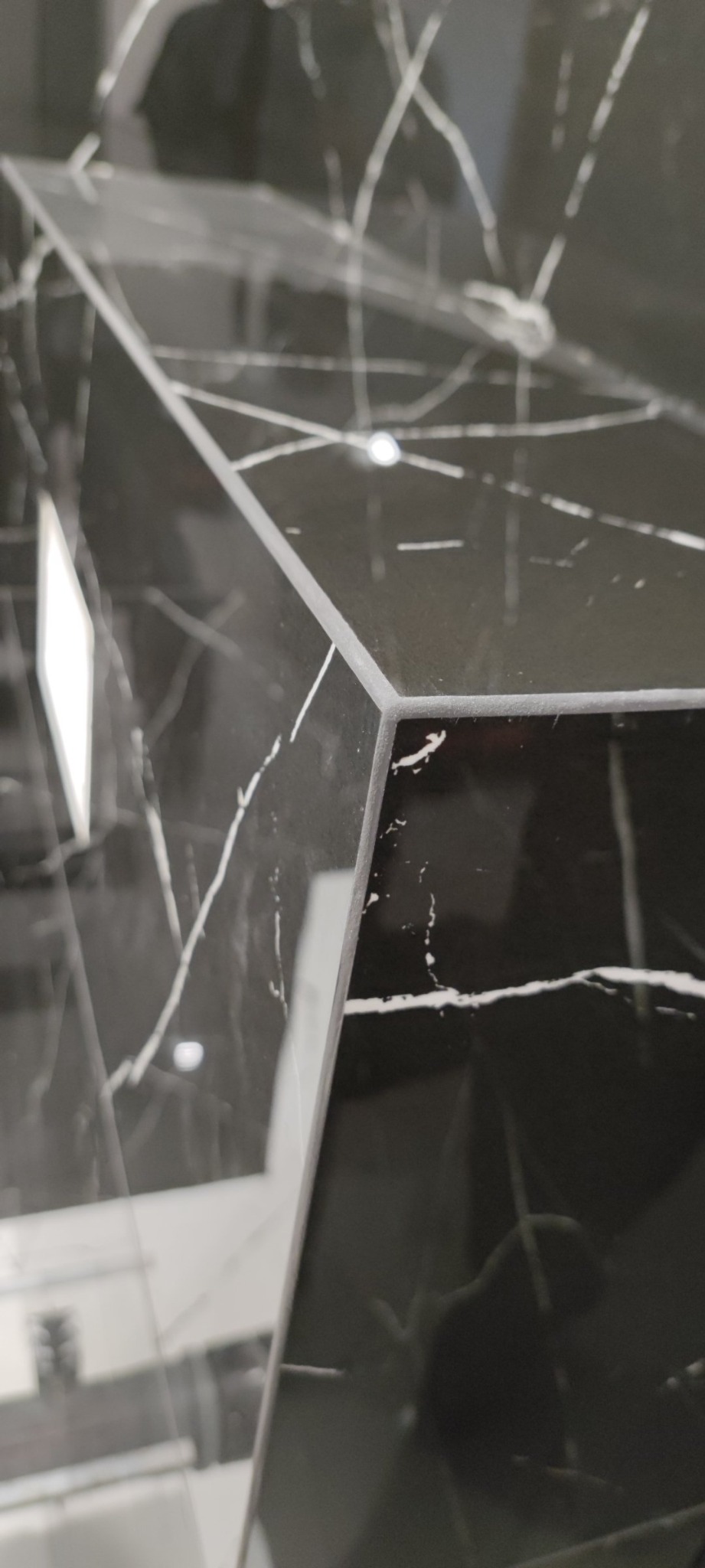 Fragment umywalki z czarnego marmuru z białymi żyłami, widoczny ostry kant i odbicie światła.