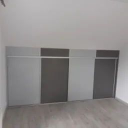 Czterodrzwiowa szafa wnękowa z przesuwnymi drzwiami w odcieniach szarości, zamontowana w pokoju na poddaszu ze skośnym sufitem i drewnianą podłogą.