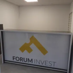 Biała lada recepcyjna z logo Forum Invest w minimalistycznym wnętrzu biurowym, oświetlona lampą sufitową.