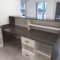 Usługowy zakład stolarski - Nowoczesna, biało-czarna szafa na wymiar z szufladami i otwartymi półkami, z czarnym blatem, widoczna w jasnym, minimalistycznym wnętrzu w trakcie montażu.