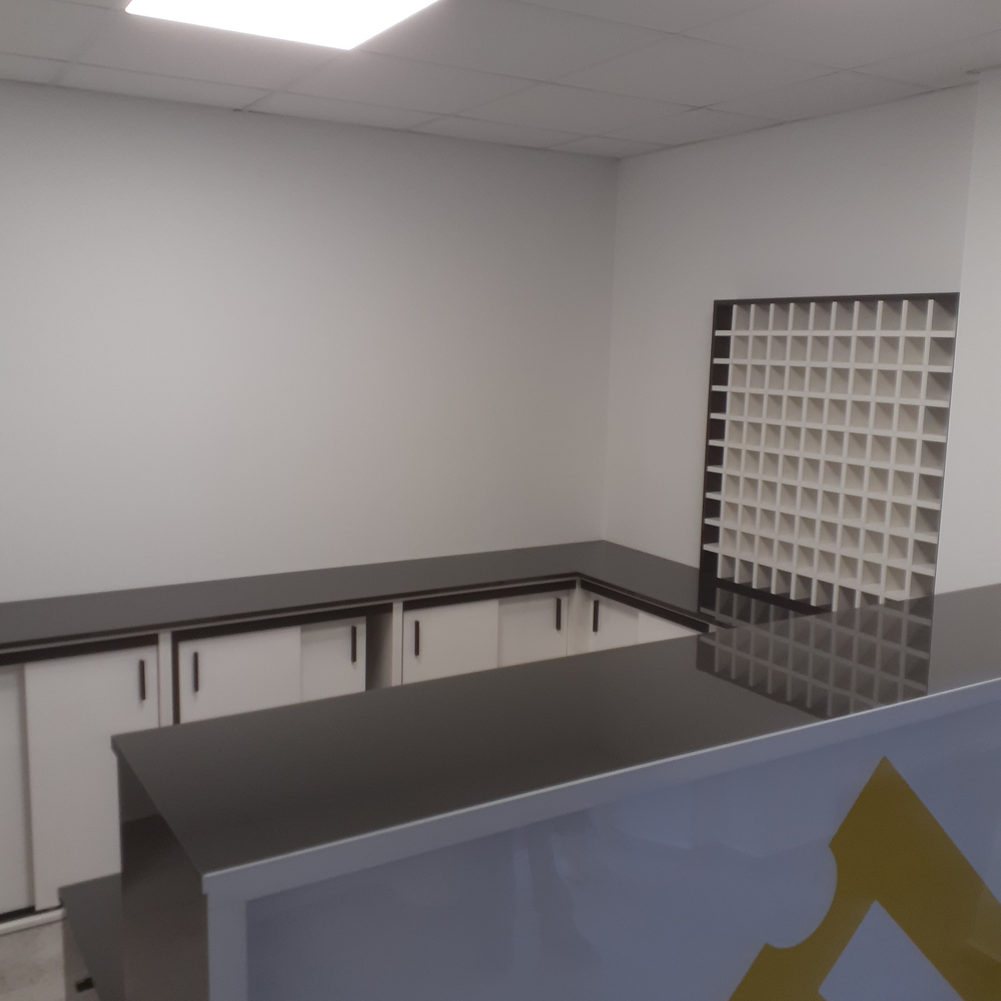 Nowoczesna zabudowa kuchenna z białymi szafkami z przesuwnymi drzwiami i czarnym blatem, uzupełniona o dekoracyjną, ażurową ściankę działową z białych kwadratów.