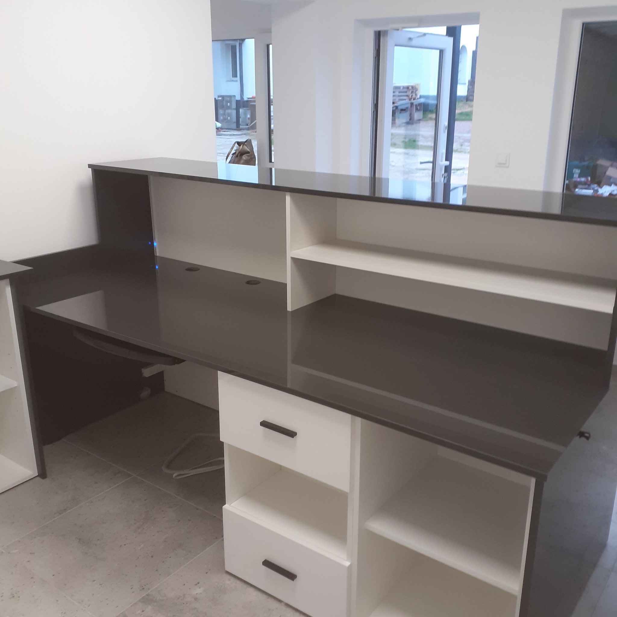 Nowoczesna, biało-czarna szafa na wymiar z szufladami i otwartymi półkami, z czarnym blatem, widoczna w jasnym, minimalistycznym wnętrzu w trakcie montażu.