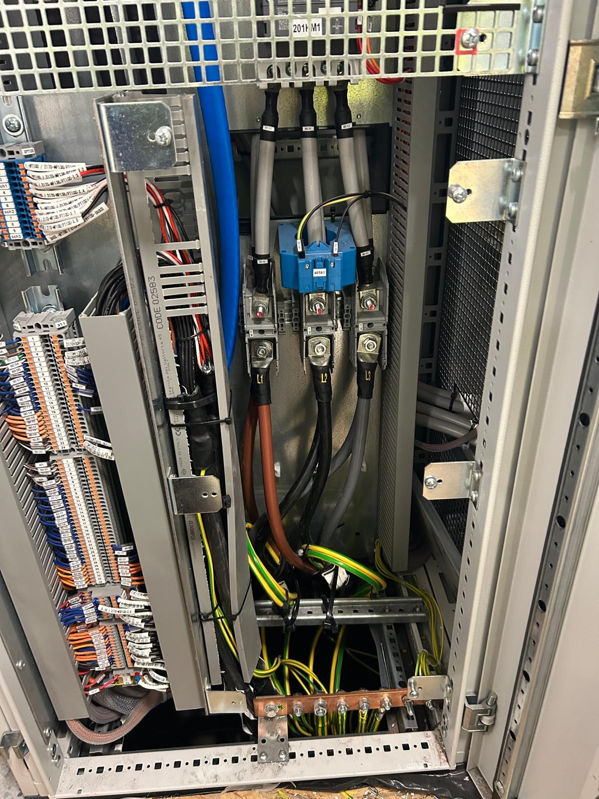 Wnętrze szafy elektrycznej z widocznymi przewodami fazowymi oznaczonymi L1, L2, L3, niebieskim transformatorem prądowym 40TA1, licznymi przewodami sterowniczymi i listwami zaciskowymi.