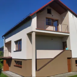 Dwukondygnacyjny dom jednorodzinny z balkonem, ocieplony i pomalowany w dwóch odcieniach beżu, z czerwoną dachówką, na tle błękitnego nieba i zieleni.