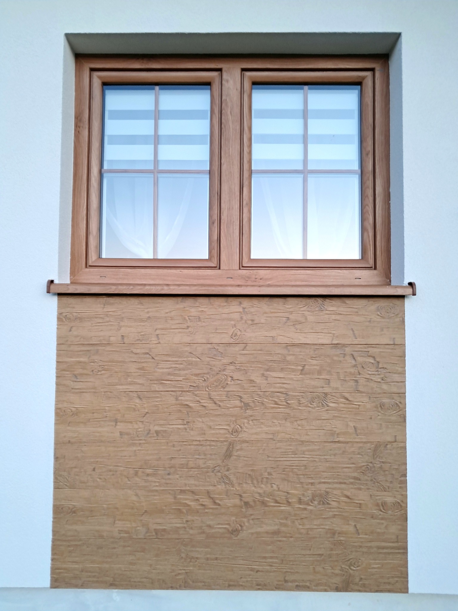 Elewacja domu z oknem w drewnianej ramie i drewnianą okładziną imitującą deski. Jasna ściana, rolety w oknie. Detal wykończenia.