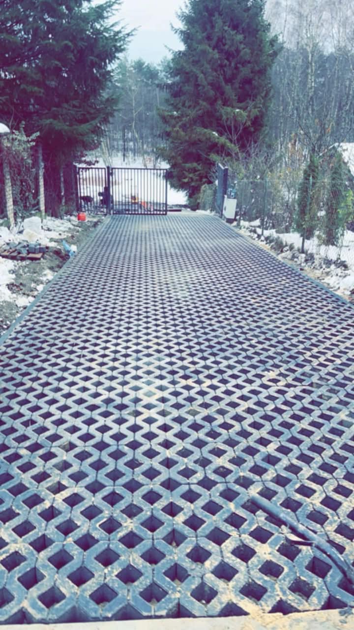 Ułożona ażurowa nawierzchnia podjazdu w zimowej scenerii, widok z dołu w kierunku bramy i drzew