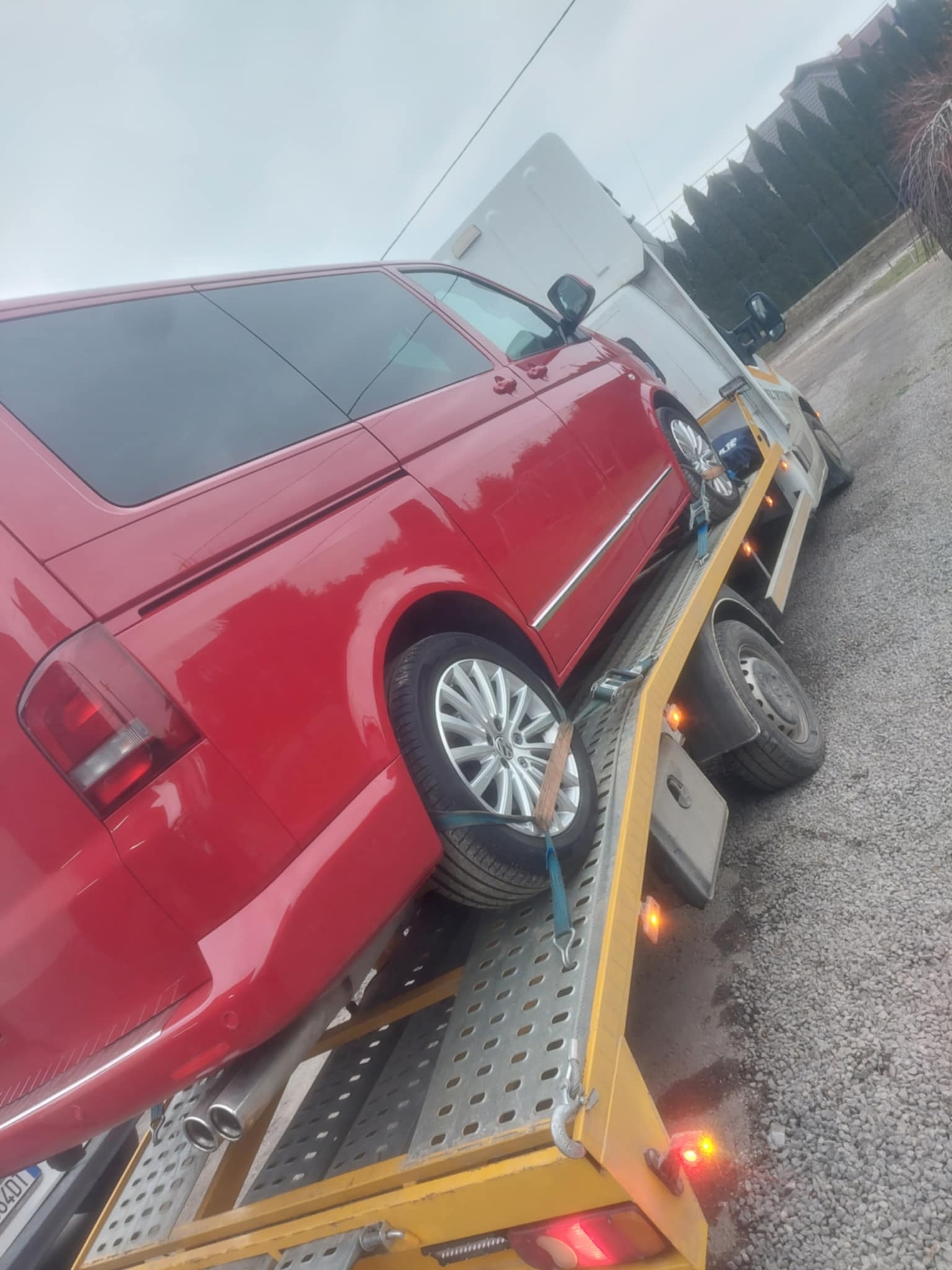 Czerwony van Volkswagen zabezpieczony pasami na żółtej lawecie, widoczne podwójne rury wydechowe i aluminiowe felgi