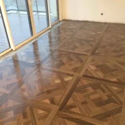 Połyskująca, wzorzysta podłoga z paneli w jodełkę, świeżo ułożona w pokoju z balkonem w Bielsku-Białej, widok na zewnątrz przez przesuwne drzwi balkonowe.