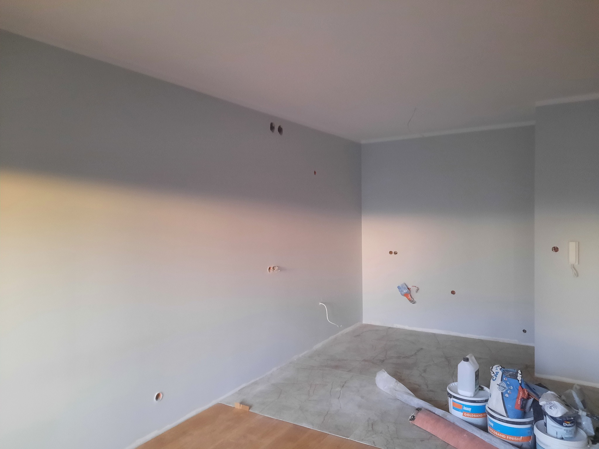 Pokój w trakcie malowania na szaro, widoczne puszki z farbą, szpachla na ścianie i przygotowane podłoże pod panele.