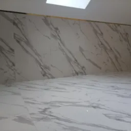 Wnętrze wykończone białymi płytami imitującymi marmur, z delikatną złotą listwą przy suficie i oknem dachowym.