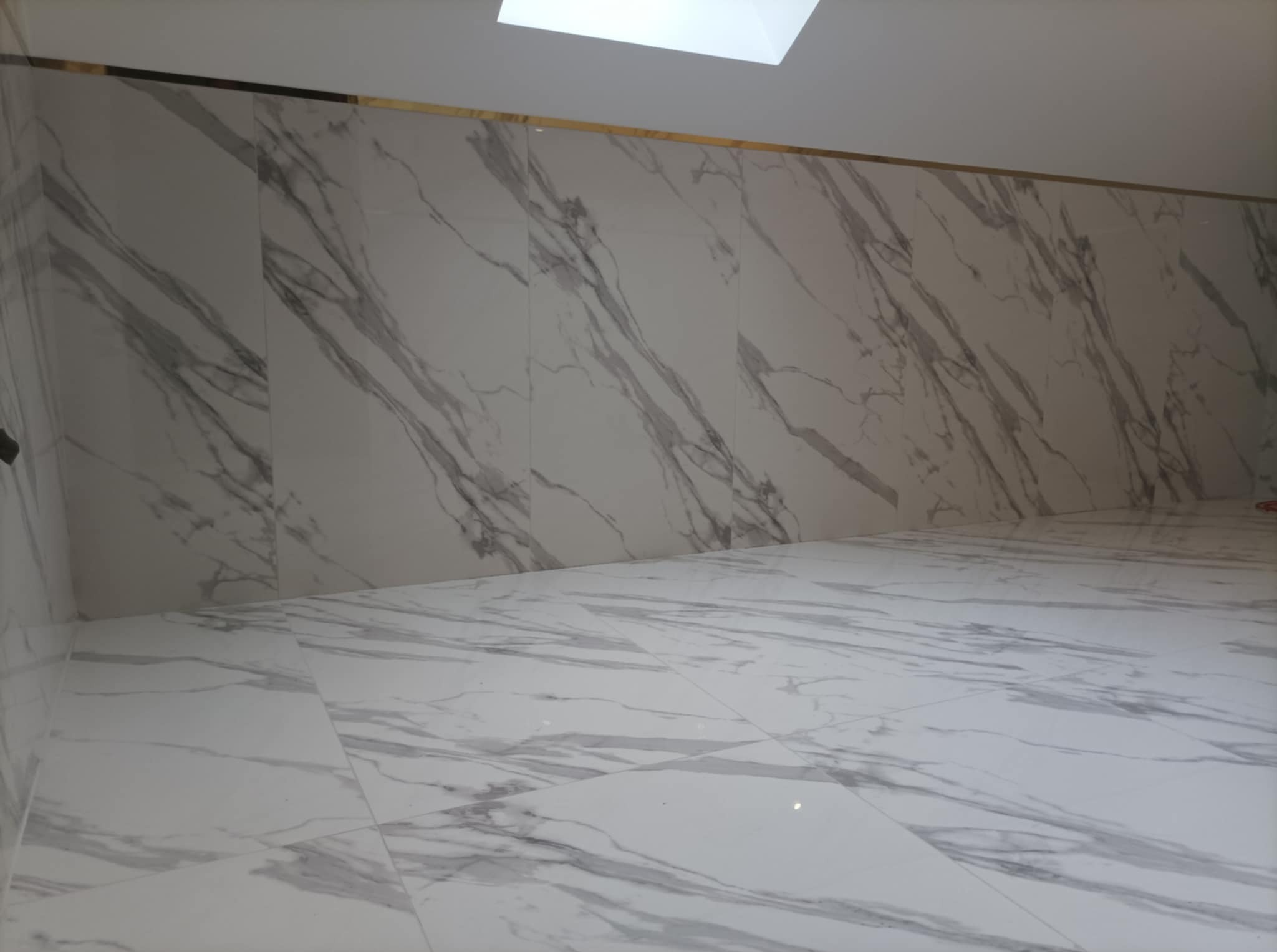 Wnętrze wykończone białymi płytami imitującymi marmur, z delikatną złotą listwą przy suficie i oknem dachowym.