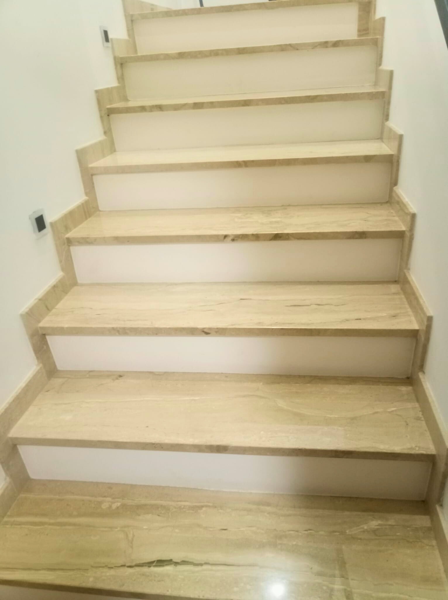 Schody wewnętrzne wykończone trawertynem z białymi podstopnicami, widok z dołu, minimalistyczny design.